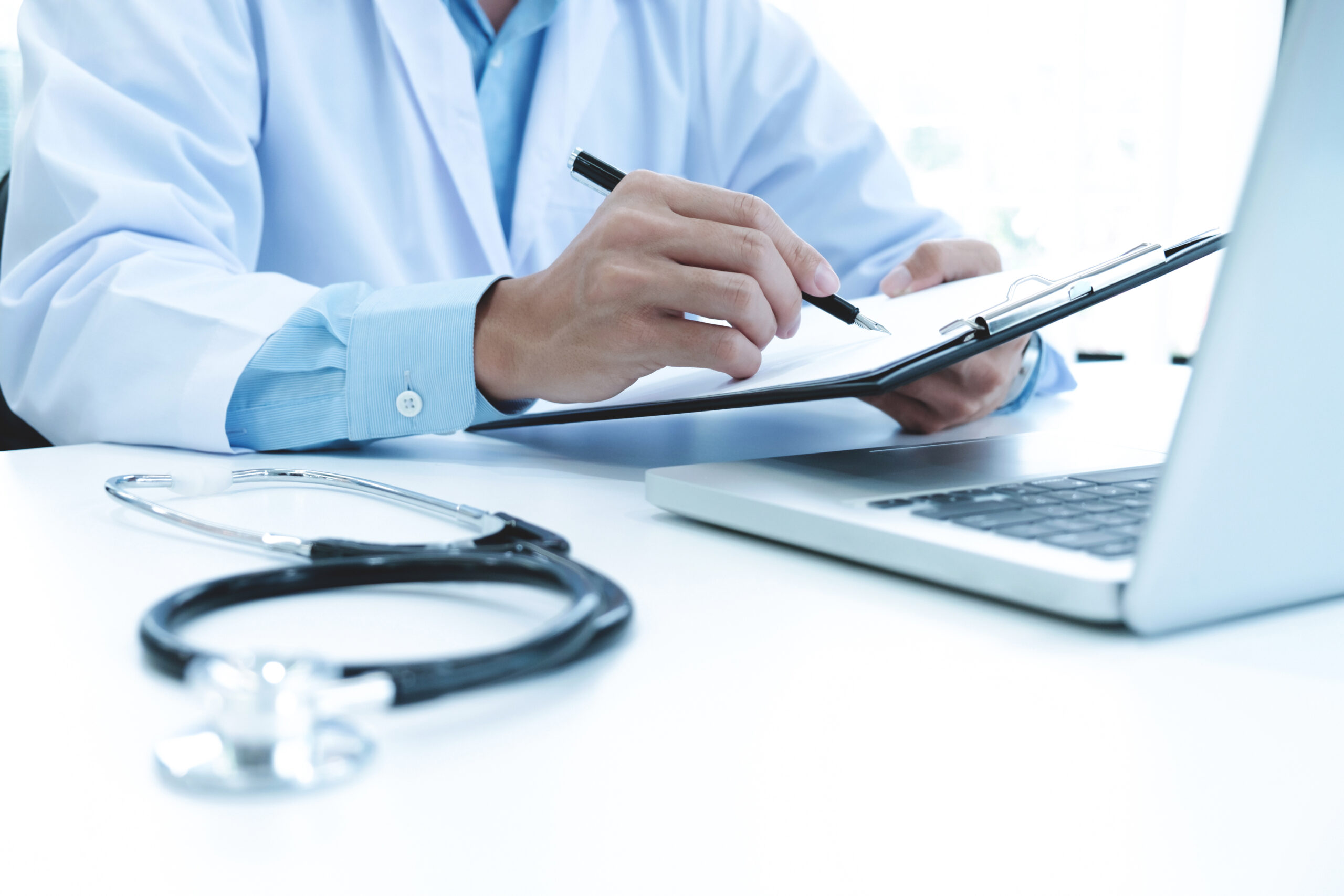 Doctor working with laptop computer and writing on paperwork. Hospital background.